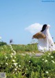 A woman in a white dress is walking through a field of flowers.